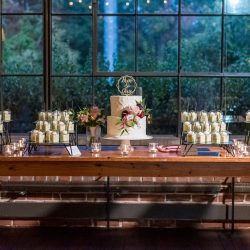 A beautiful white wedding cake with different desserts in cups on the tale