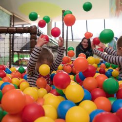 Young mom plays with her kids at pool with colorful balls in a children's playroom